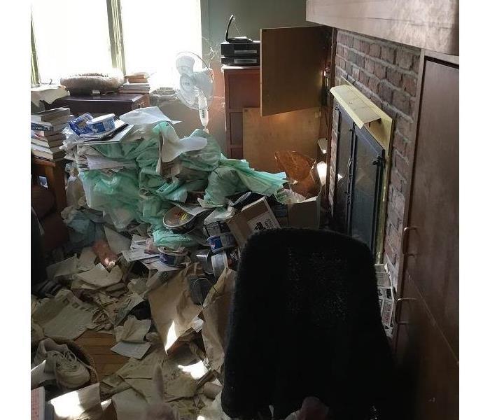 A debris-covered living area near a fireplace covered in various papers and other waste
