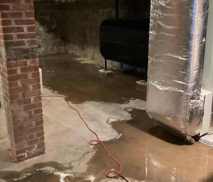 Unfinished basement with a wet concrete floor and exposed duct board HVAC