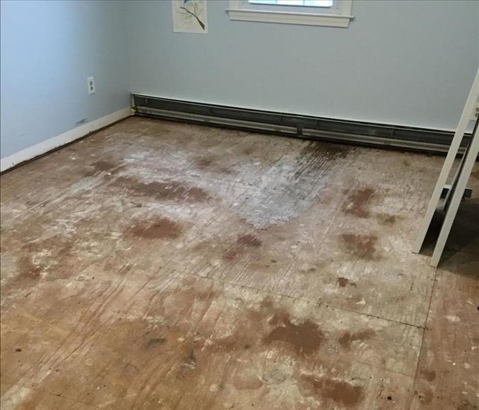 A room with an exposed subfloor and heavy water damage on the boards