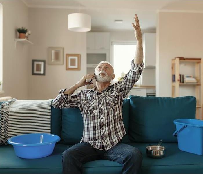 man with two buckets catching water leaking from ceiling