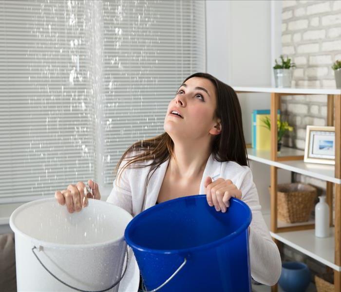 woman holding two buckets, leaking ceiling